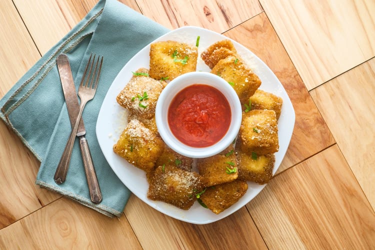 Aerial view of breaded fried ravioli around a bowl of sauce