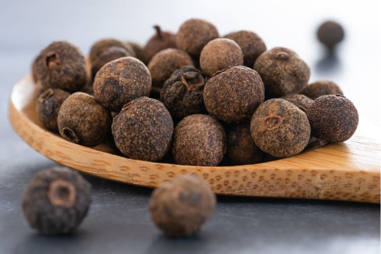 Allspice berries tipping out of wooden spoon