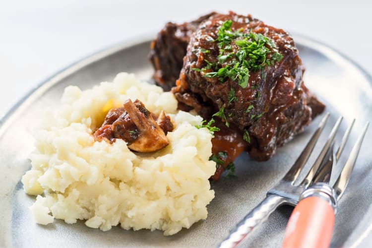 Braised short ribs with garnish on top next to mashed potatoes