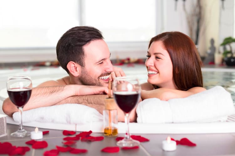 A couple in a hot tub with red wine glasses on the side