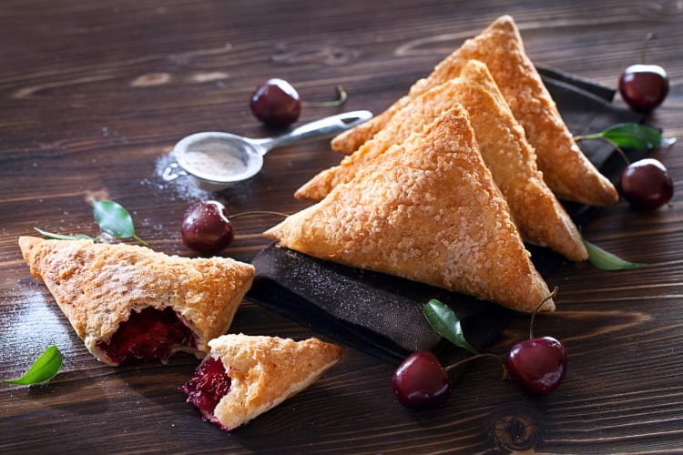 Four puff pastry cherry turnovers, one with a piece broken off