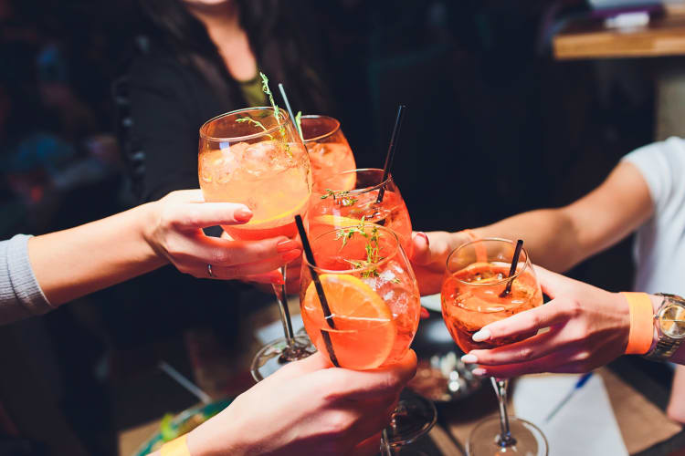 Five friend's hands clinking glasses of Aperol Spritz together