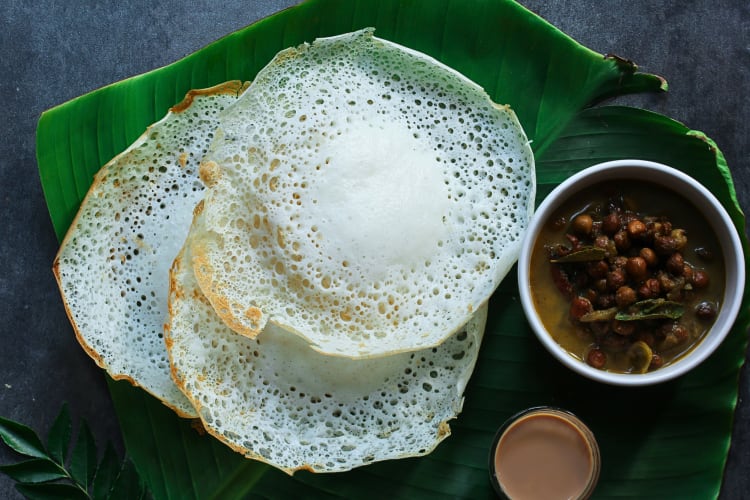 Three portions of appam with kadala curry tea on a banana leaf