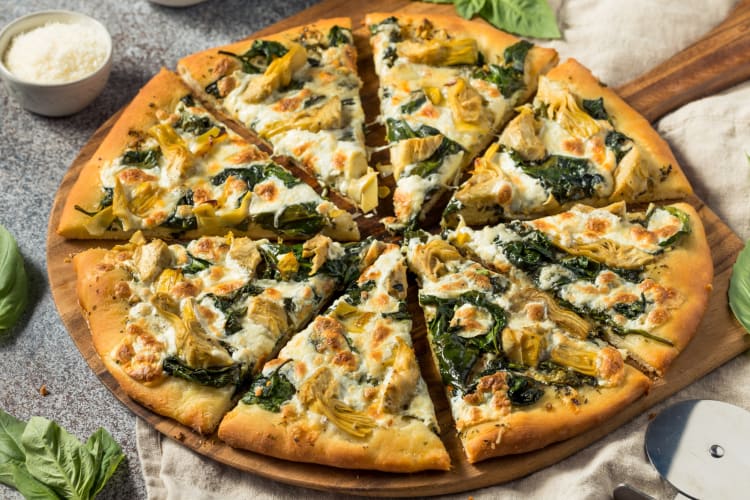 An artichoke spinach pizza served on a wooden board