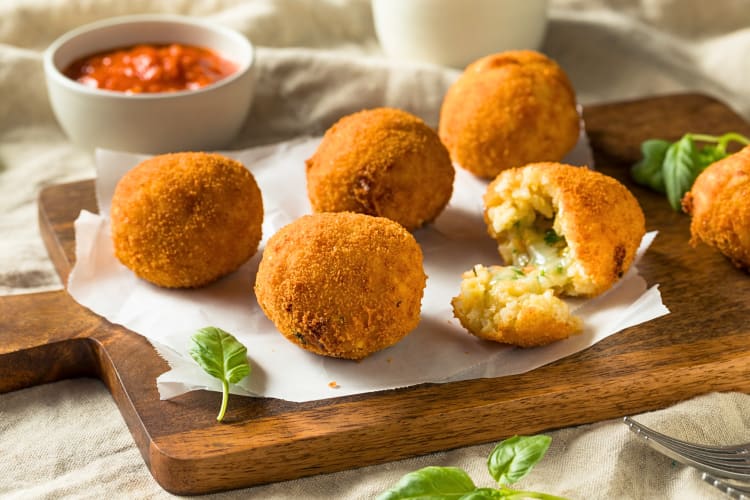 Arancini balls on a wooden serving board, in front of a bowl of sauce