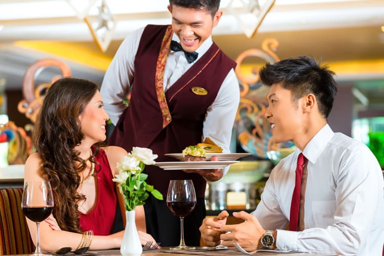 A waiter serving food to a couple at an Asian restaurant