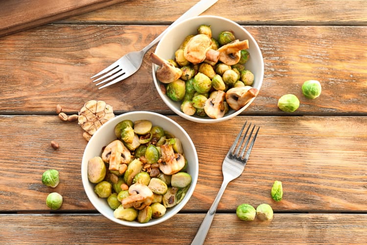 Aerial view of two bowls filled with Brussels sprouts and mushrooms, next to two forks