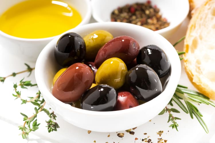 A bowl of mixed olives next to olive oil and bread