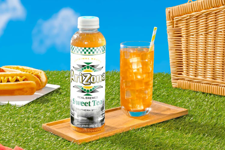 A bottle of Arizona Sweet Tea next to a glass of iced tea, a picnic hamper and a hot dog