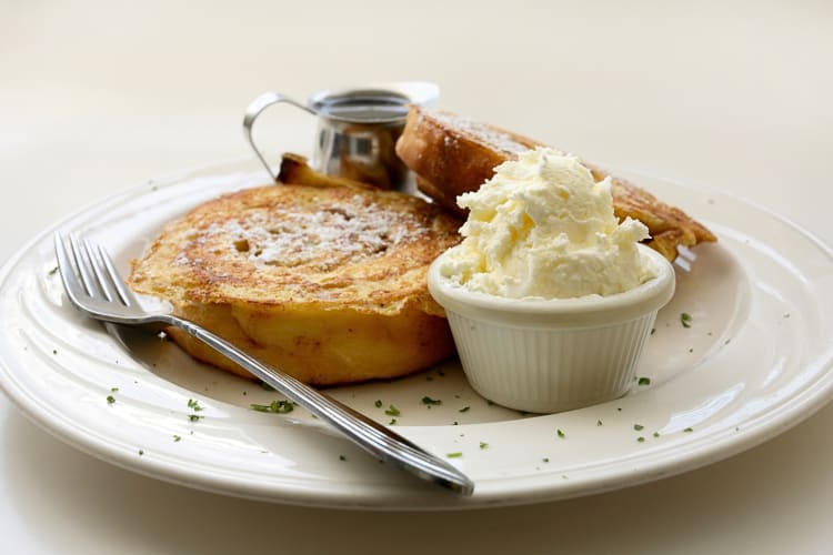 Cinnamon roll French toast on a plate with ice cream and a jar of syrup
