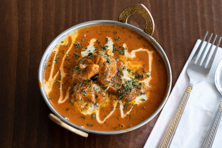 Butter chicken with garnish on top next to a fork, spoon and handkerchief