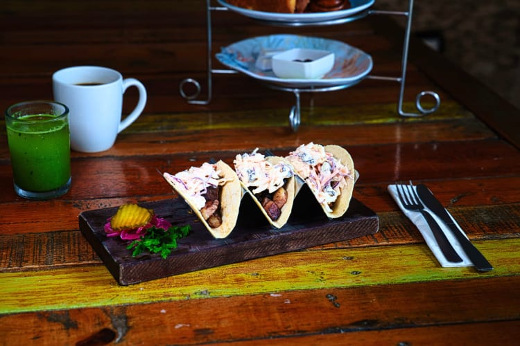 Three tacos, next to a coffee and green juice, from Así Restaurant & Beach Club