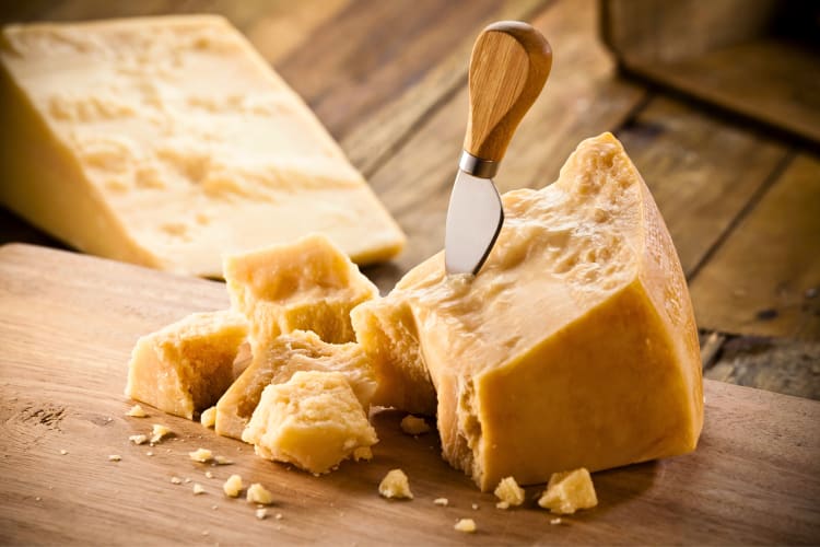 Block of parmesan cheese with a knife wedged in it, on a chopping board