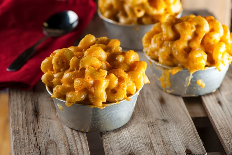 Three portions of macaroni and cheese in small bowls next to a spoon and napkin