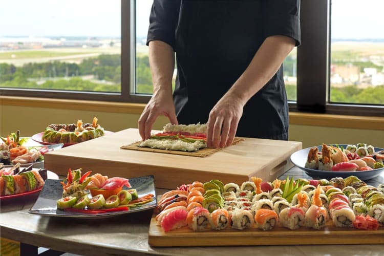 Hands of a chef making sushi, surrounded by platters of sushi