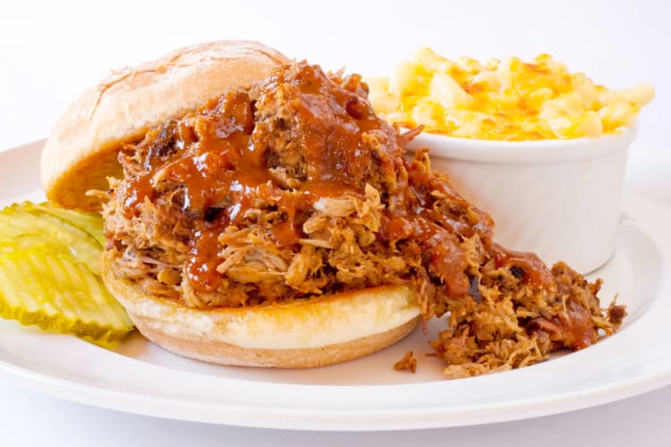 A pulled pork sandwich next to pickles and mac and cheese