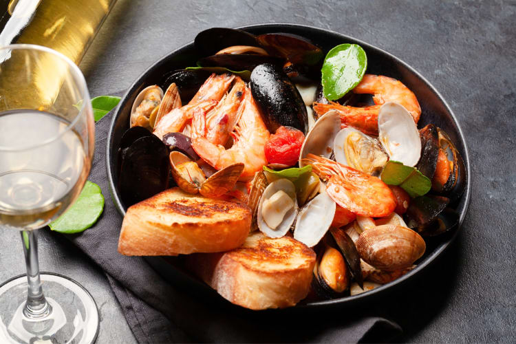 Seafood mixed grill served in a black bowl next to a glass of wine