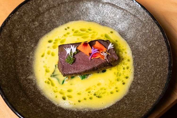 Aerial view of a piece of meat on a bed of yellow sauce, from Aurora Restaurant at Ila