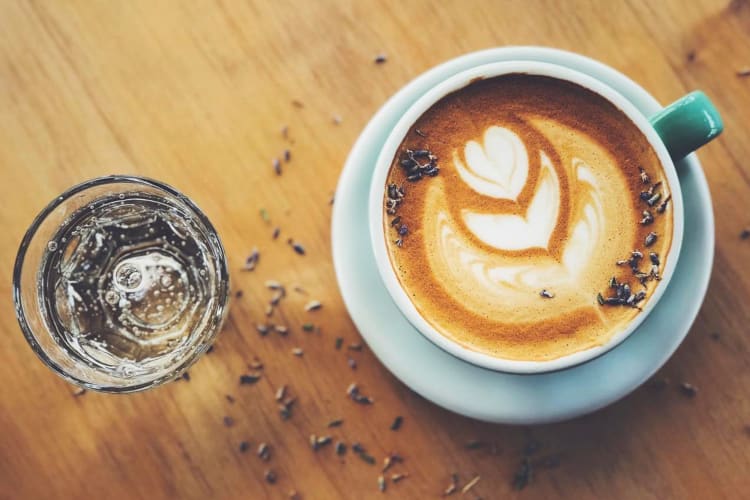 A cup of coffee with latte art next to a glass of water