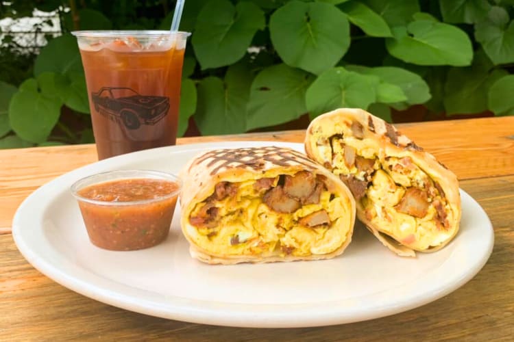 A breakfast burrito on a plate with salsa next to a red drink