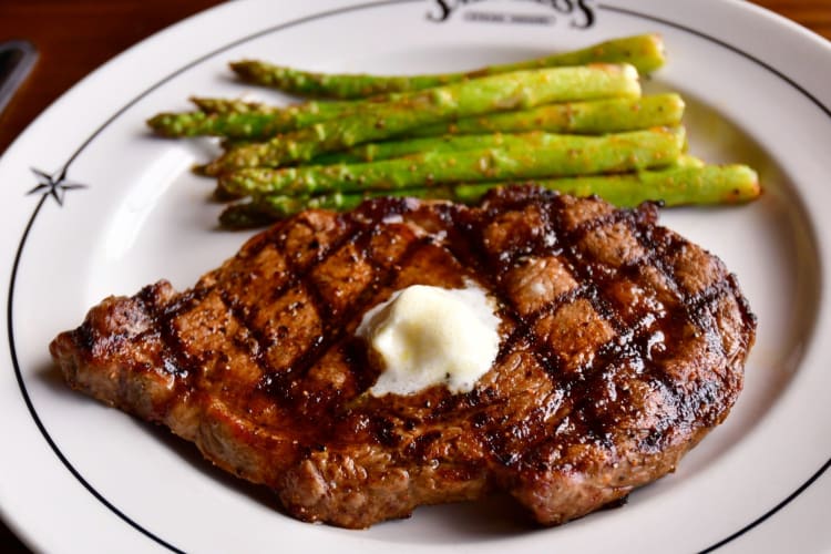 A steak topped with butter and served with asparagus