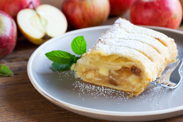 A portion of Viennese apfelstrudel on a plate next to fresh apples