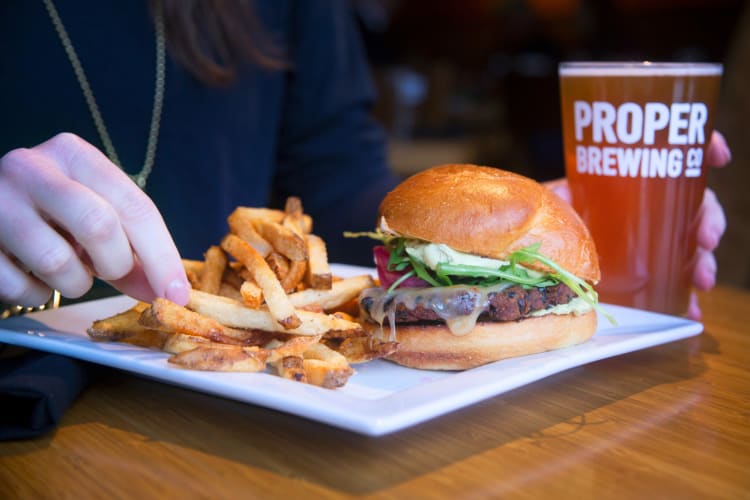 Person's hand reaching for chips, next to a burger and beer from Avenues Proper