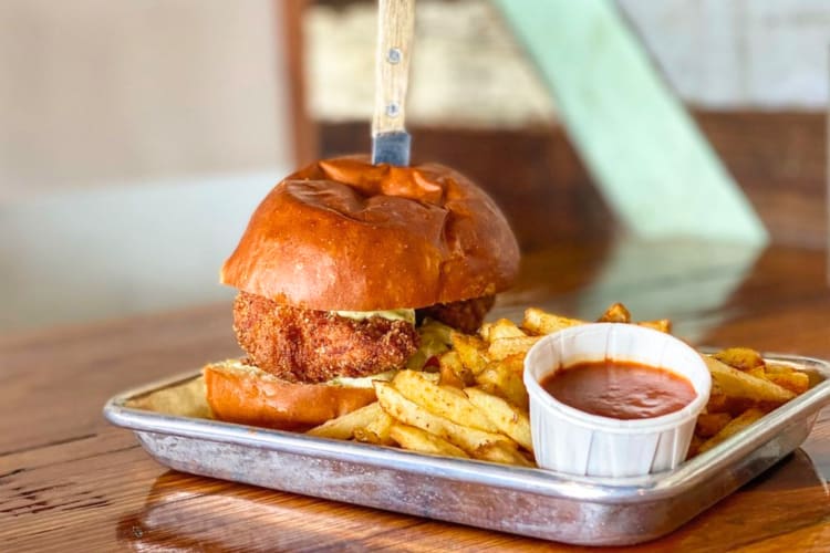 A thick fried chicken sandwich with fries and tomato sauce. 