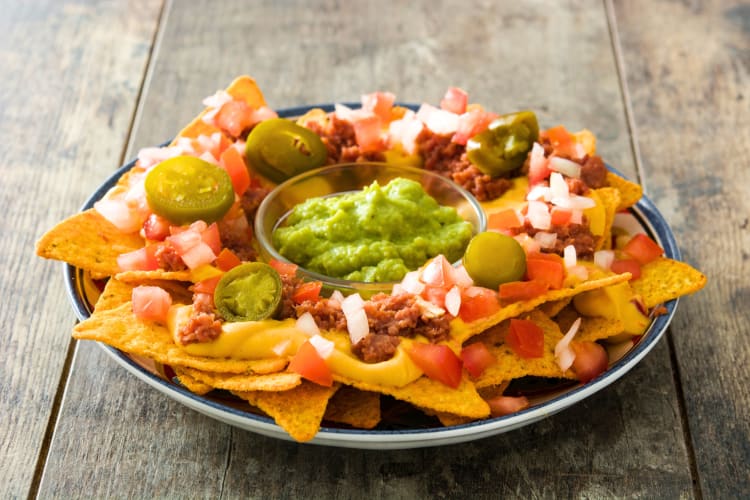 A plate of nachos topped with jalapeño peppers, minced beef, onions and has guacamole at the center. 