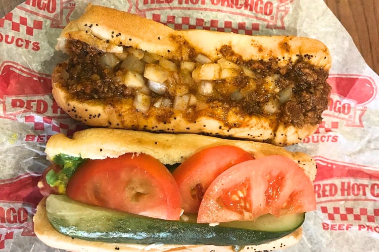 A hot dog stuffed with tomatoes and cucumbers and a beef hot dog topped with onions. 