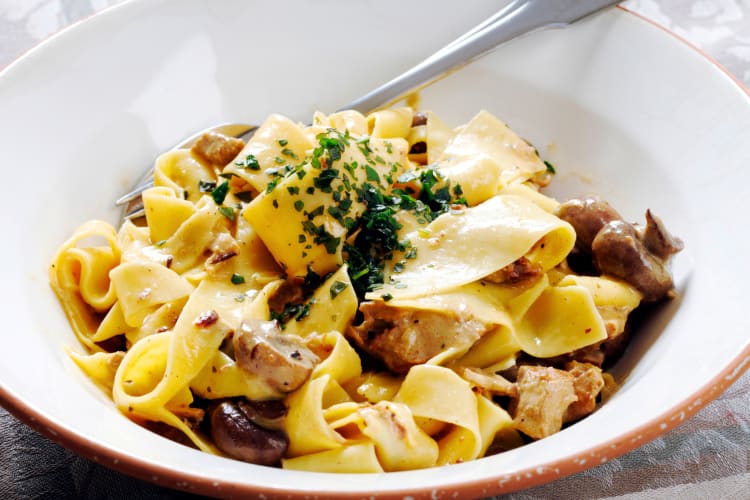 Pappardelle al Cinghiale is a type of Italian pasta. This one is served in a white bowl with mushrooms mixed into the dish. 