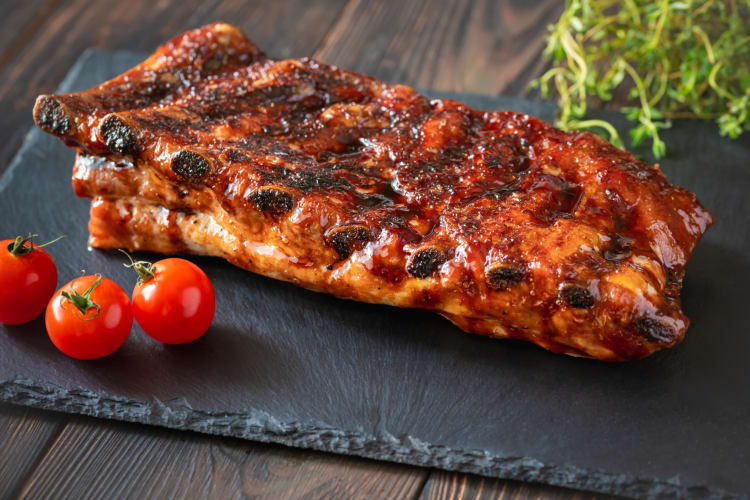 Portion of ribs ready to be eaten with tomatoes and green herbs on the side