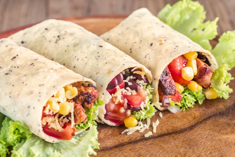 Three burritos on a wooden board ready to be eaten