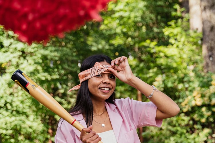 a woman smiles at the camera with a pinata in view and a bat in hand