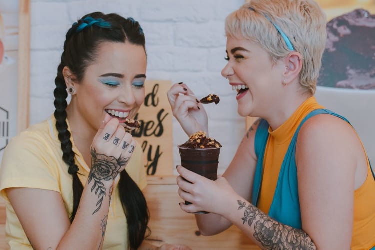 two women laugh together as they share a chocolate dessert