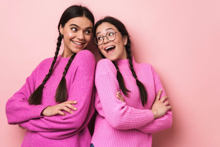 Two friends standing back to back in front of a pink background