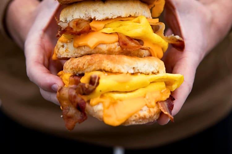 Person's hands holding two Carl's Jr. breakfast bacon, egg and cheese biscuits