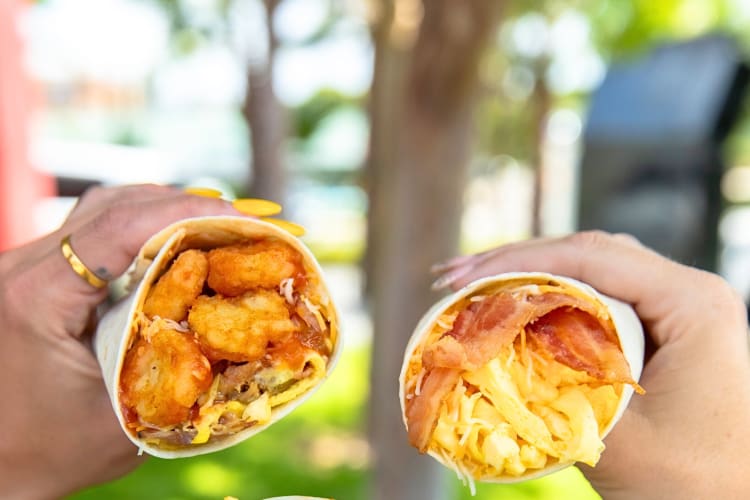 Two hands holding two Carl's Jr. breakfast burritos
