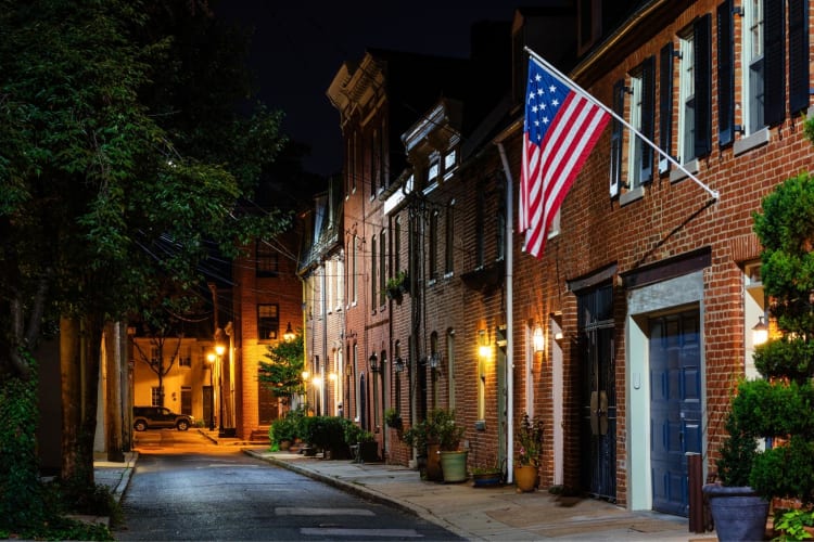 A side street with brick houses and an American flag at night