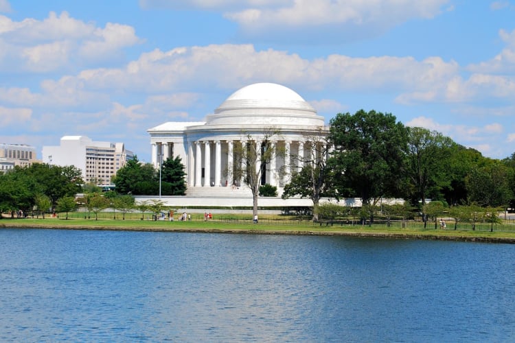 A round white building with columns and a dome next to water and trees