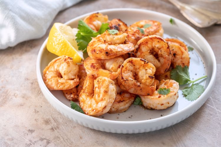 Portion of shrimp with garnish and lemon wedges in a white bowl