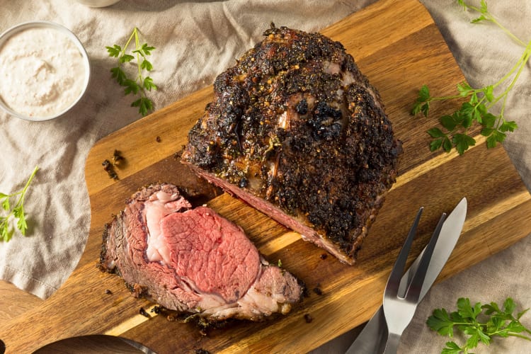 Aerial shot of a slice of prime rib next to a larger piece on a chopping board