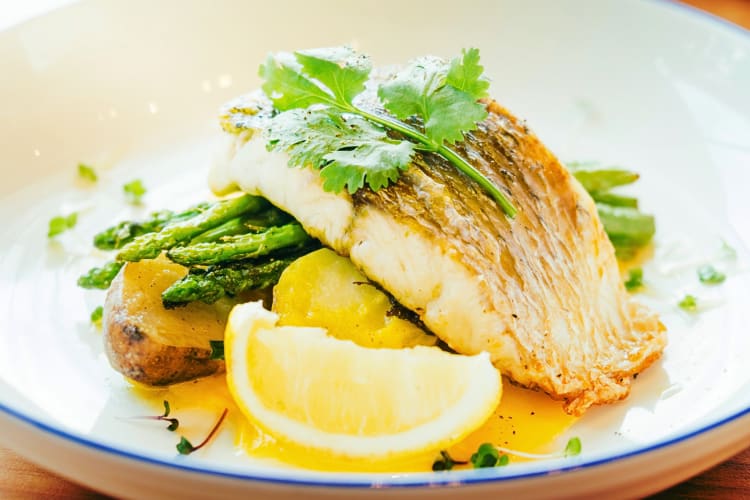Grilled barramundi on a plate with asparagus, potatoes and a lemon wedge