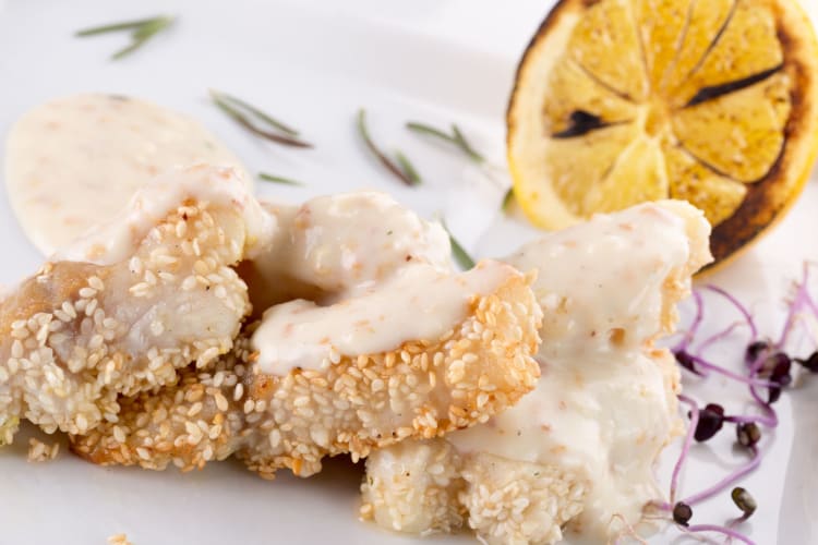 A piece of white fish coated in sesame seeds and served with a lemon butter sauce.