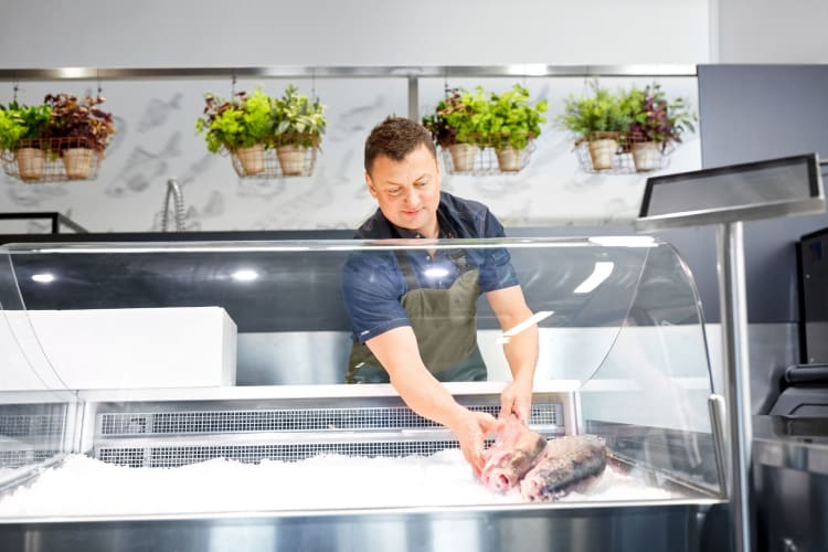 A fishmonger lays fish out in the shop's freezer display cabinet.