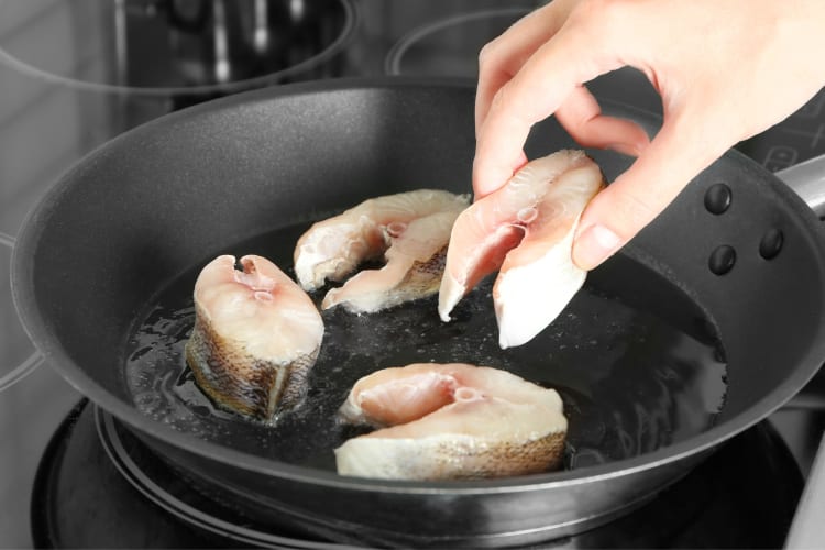 A person putting white fish into a frying pan