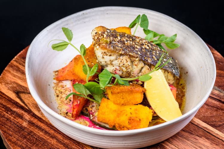 A beautiful piece of oven-baked barramundi served with roasted vegetables and a lemon wedge.