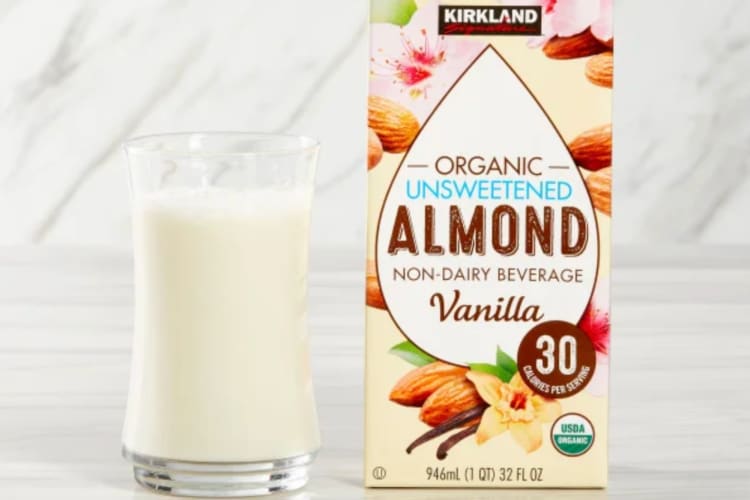 A carton of Kirkland vanilla almond milk next to a glass of almond milk