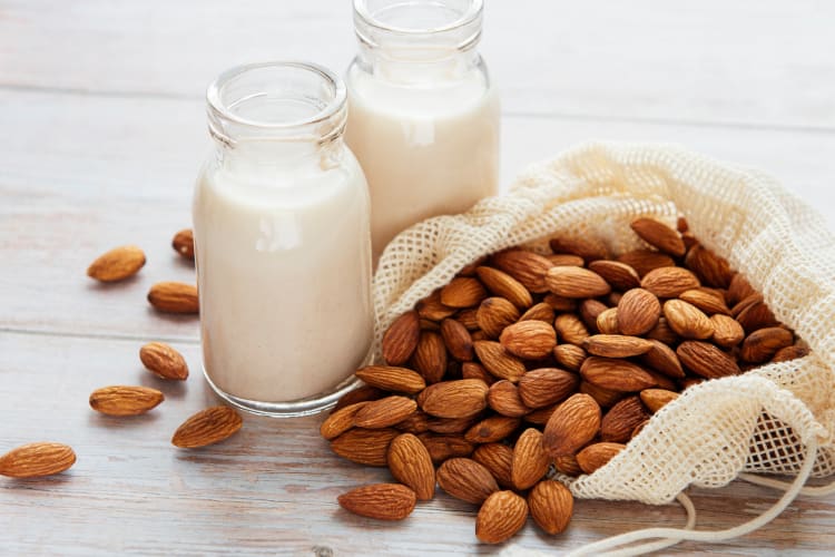 Almond milk in a glass bottles next to fresh almonds