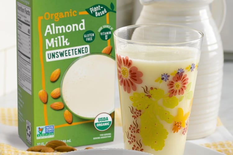 A glass of milk next to a green almond milk carton